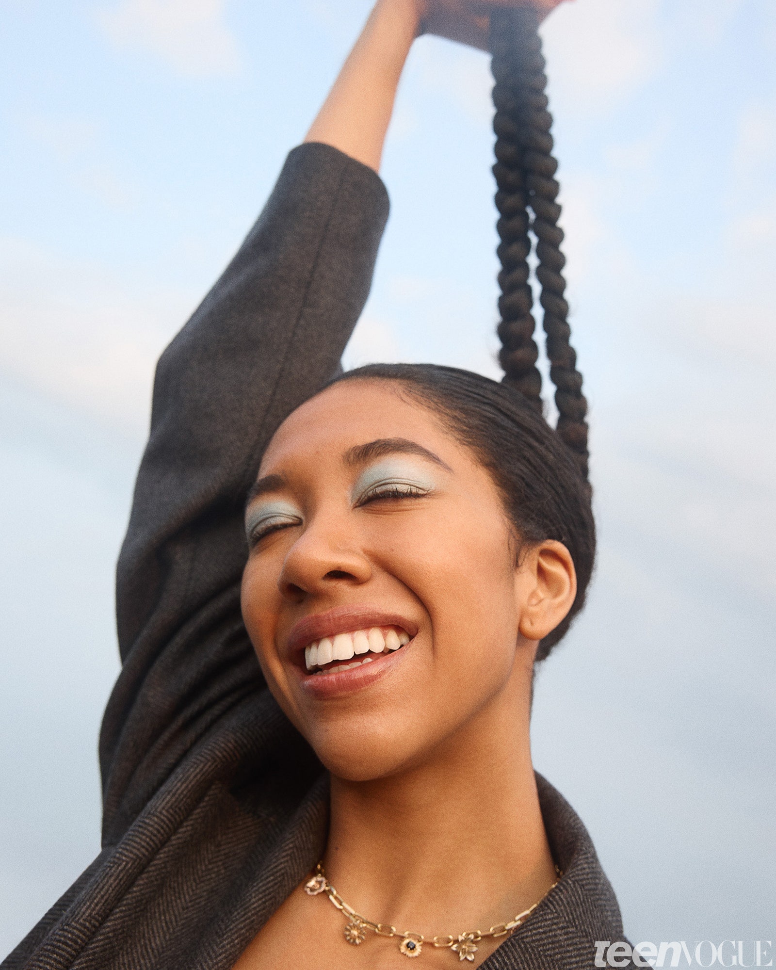 Aoki Lee Simmons smiling holding her ponytail up against the sky.