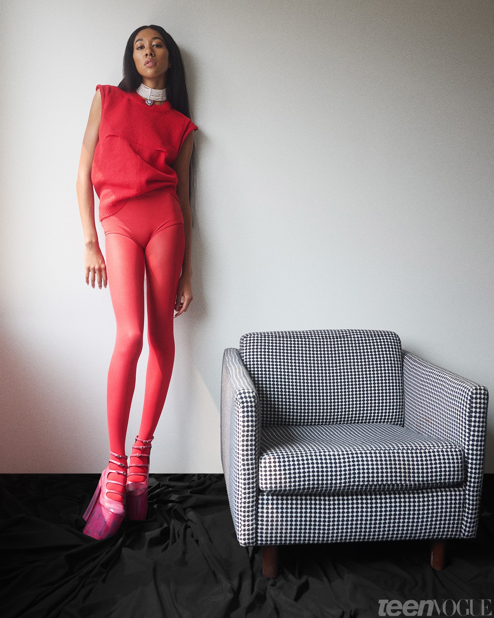 Aoki Lee Simmons wearing all red standing next to a loveseat.