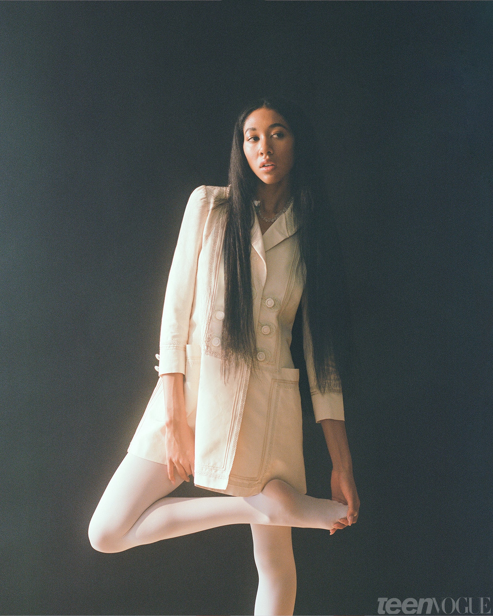Aoki Lee Simmons standing in white dress holding her foot.