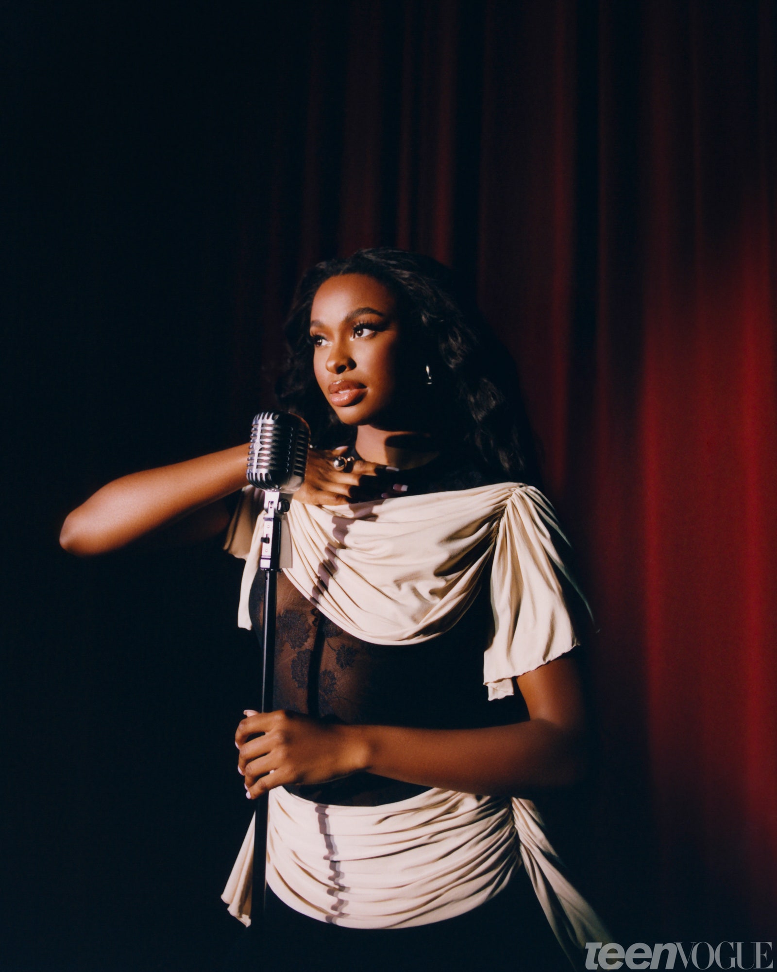 Coco Jones holding a microphone in front of a red theater curtain