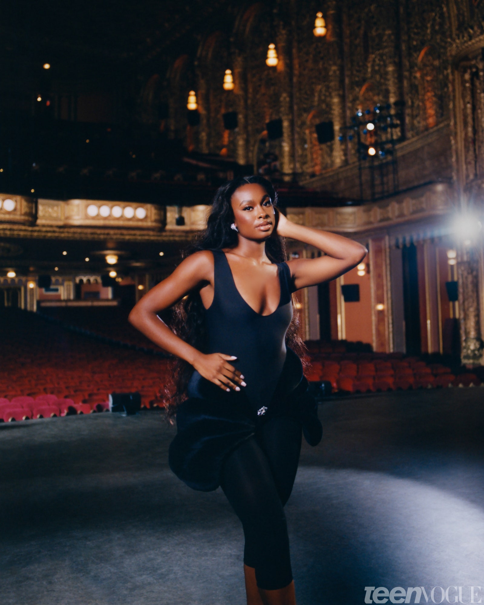Coco Jones standing on a theater stage with her back to the audience