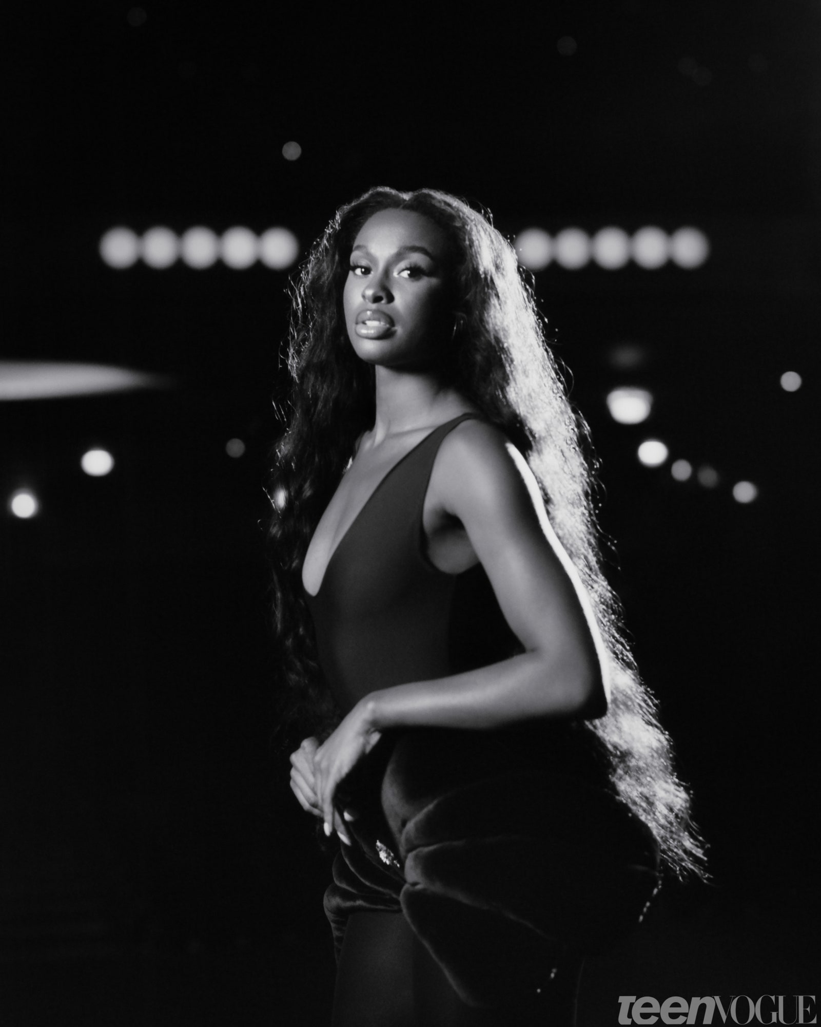 Coco Jones in black and white standing on a dark theater stage
